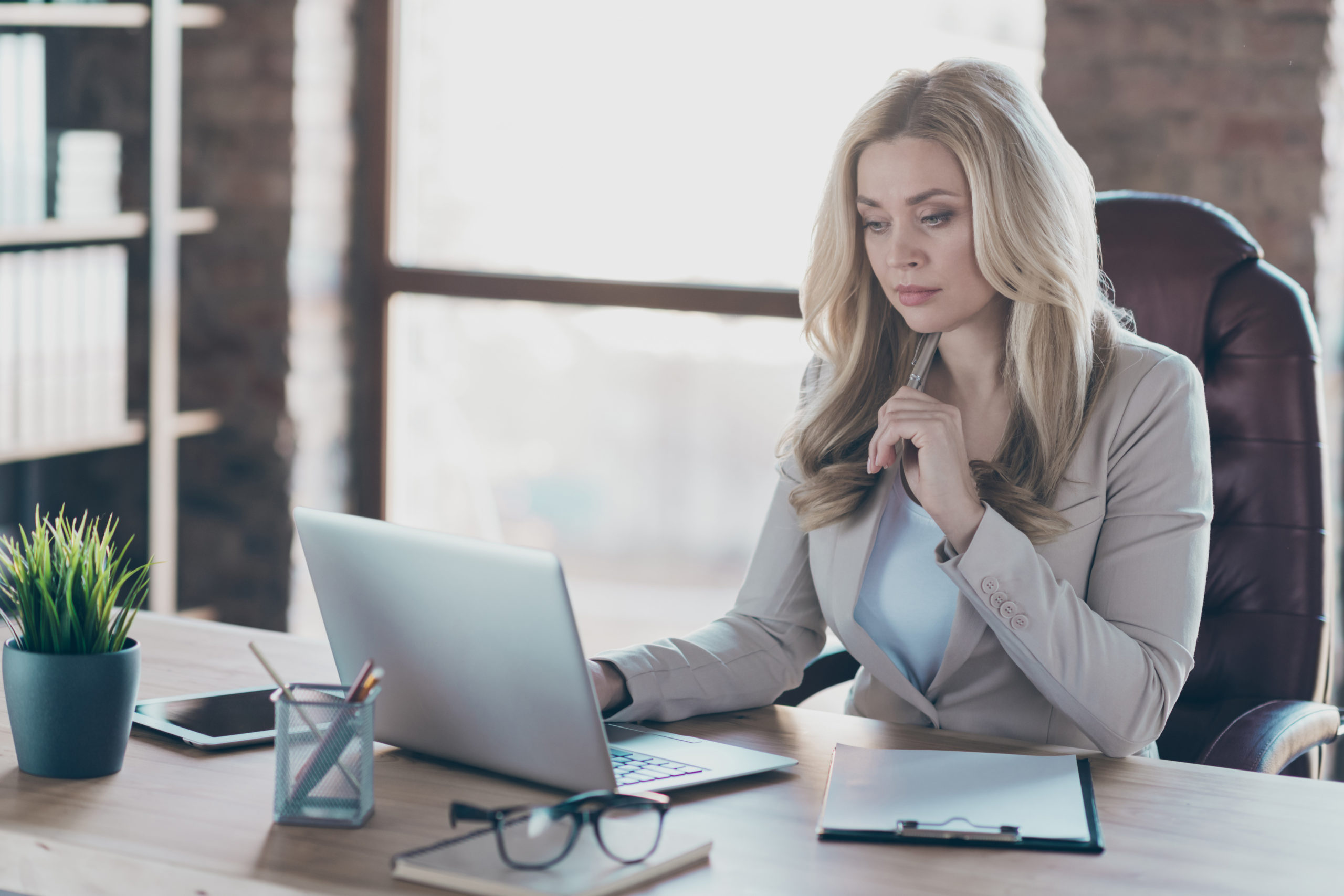 Berufsunfähigkeit Berufe: blonde Geschäftsfrau, die an einem Schreibtisch vor ihrem Laptop sitzt.